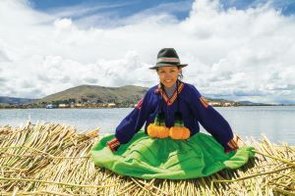 Ein lächelndes Mädchen sitzt auf einer schwimmenden Uros-Insel am Titicacasee in Peru.